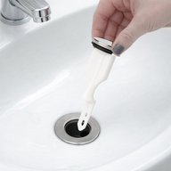 A hand dropping a white pop-up stopper with a chrome cap into a bathroom sink drain opening