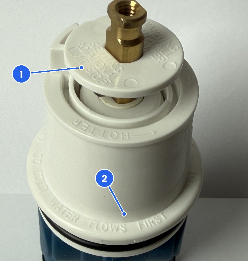 Photo of the top of a FourHome replacement cartridge for Delta RP19804 with two numbered markers: 1 the rotational limit stop disc, 2 the molded rim marking that says cold water flows first
