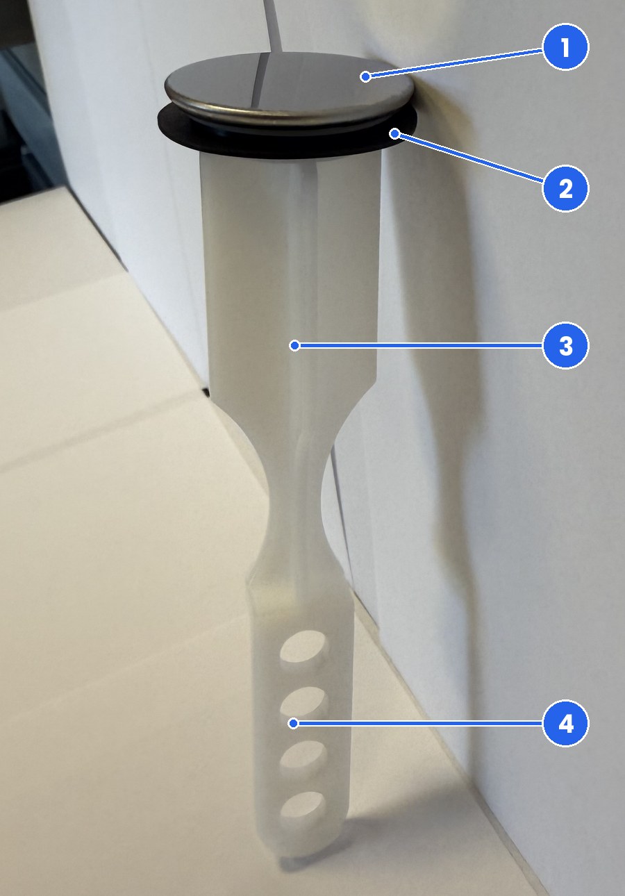 Real photo of the FourHome pop-up sink stopper standing on a white surface, showing the round metal cap, the black rubber ring under the cap, the white molded body and the strip at the foot with a row of round holes, each marked with a number